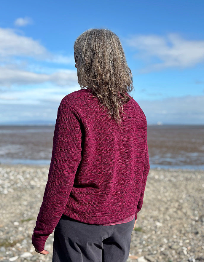 Person wearing a maroon sweater standing on a beach with a blue sky and clouds in the background.