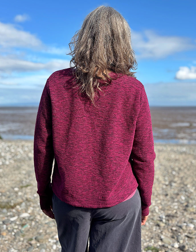 Person wearing a maroon sweater standing on a beach with a blue sky.