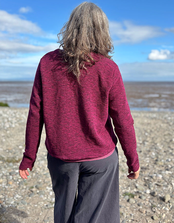 Person wearing a maroon sweater standing on a beach with a blue sky and clouds in the background.