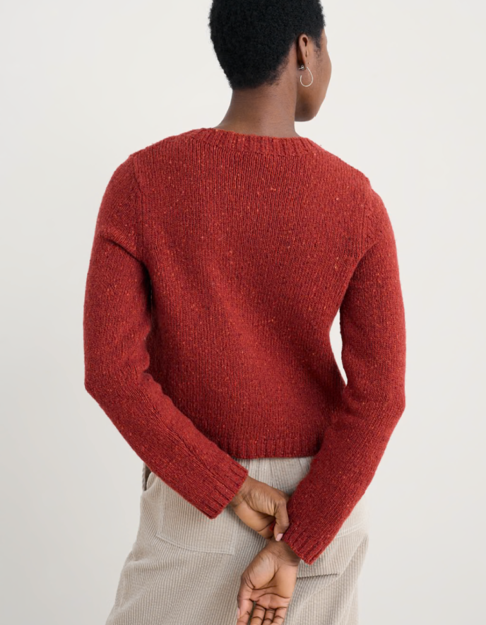 Person wearing a red knitted donegal tweed cardigan with a neutral background