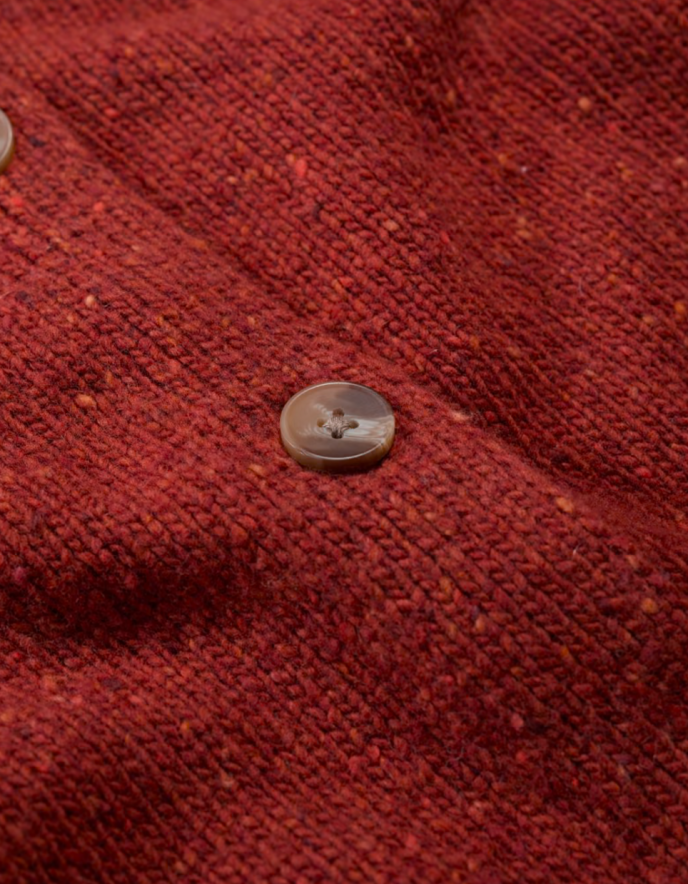 Person wearing a red knitted donegal tweed cardigan with a neutral background