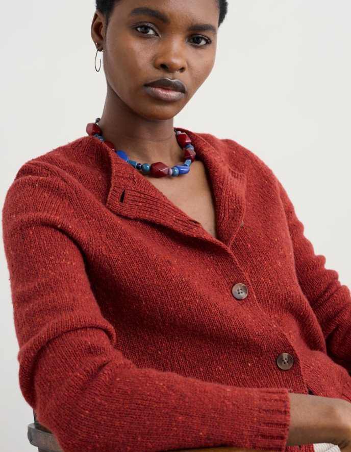 Person wearing a red knitted donegal tweed cardigan with a neutral background