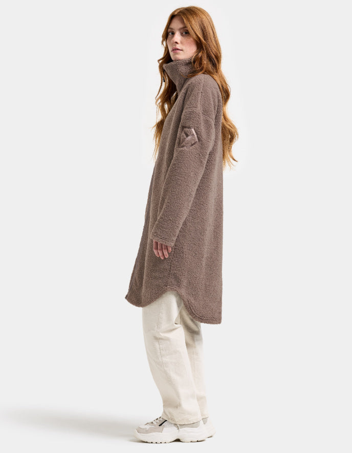 Woman wearing a brown long sherpa pile fleece coat on a white background
