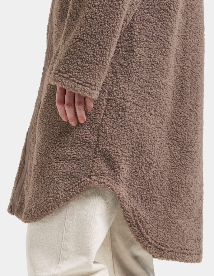 Woman wearing a brown long sherpa pile fleece coat on a white background