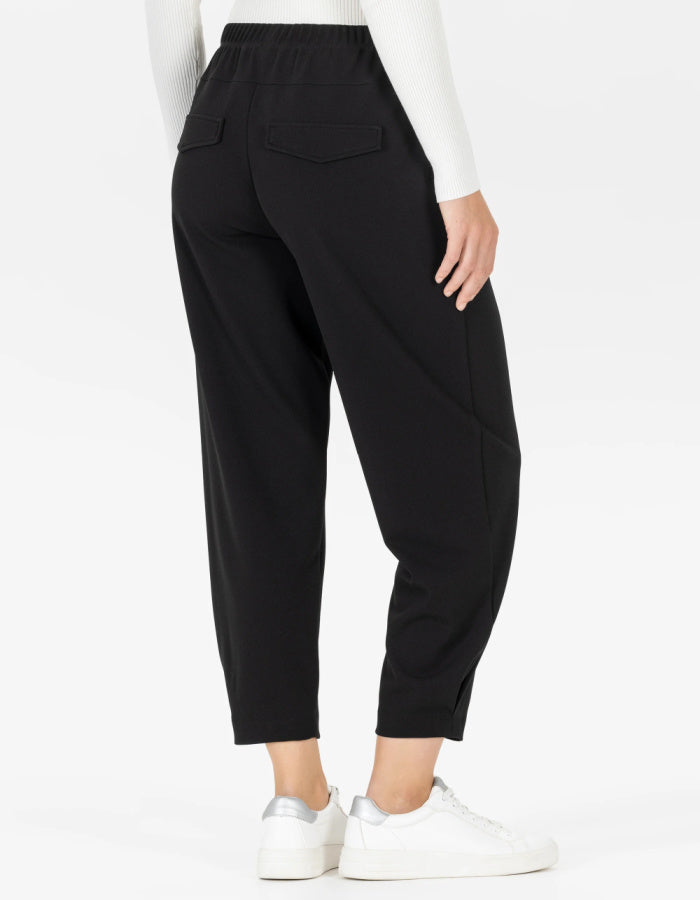 Black cropped pants with an elastic waistband and side pockets, shown on a model from the back wearing white sneakers against a plain white background.