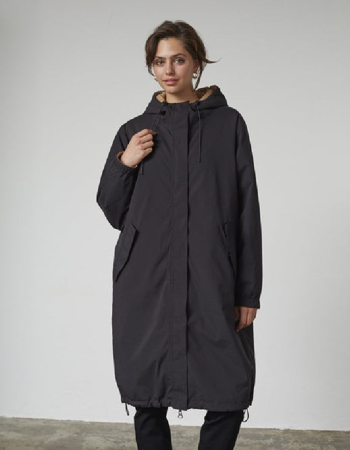 Woman wearing a black and beige reversible winter coat against a plain background