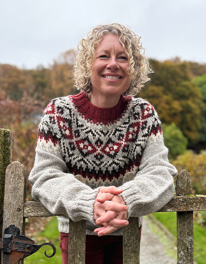 Woman wearing a patterned sweater standing behind a wooden gate with a natural background