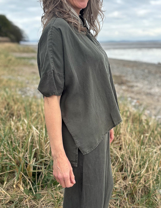Person standing in a field wearing a green tencel oversized shirt, co - ord pants, and red sneakers.