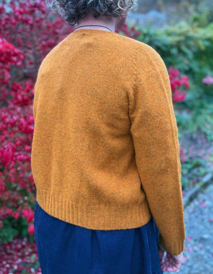 Person wearing a mustard yellow sweater with a blurred background of pink flowers and greenery