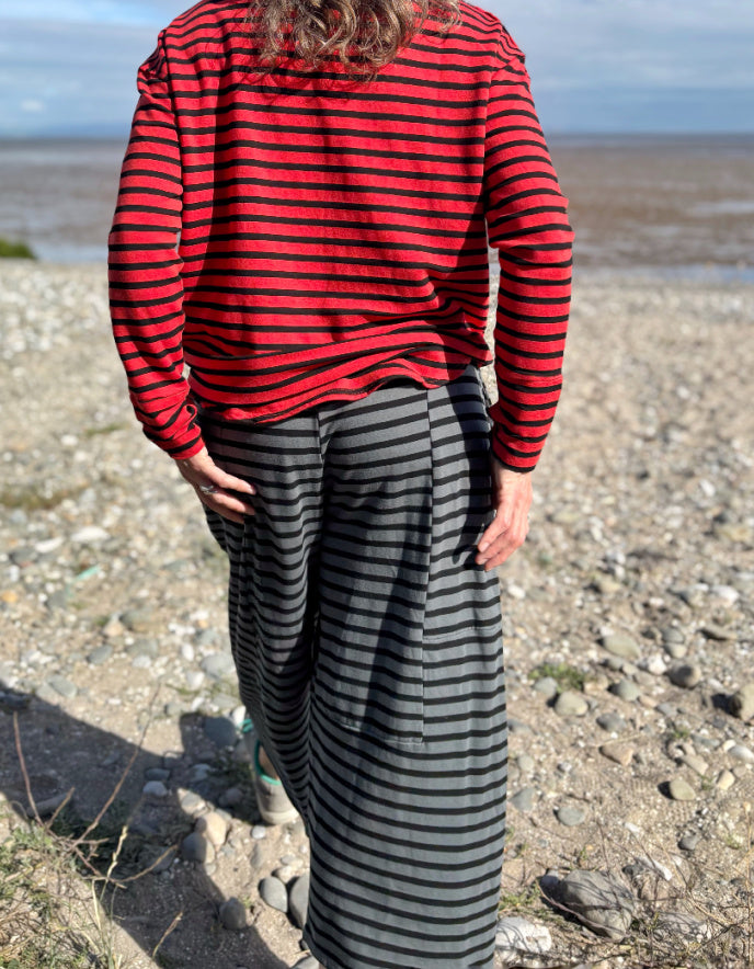 Person wearing a red and black striped shirt and gray pants standing on a pebbly beach.