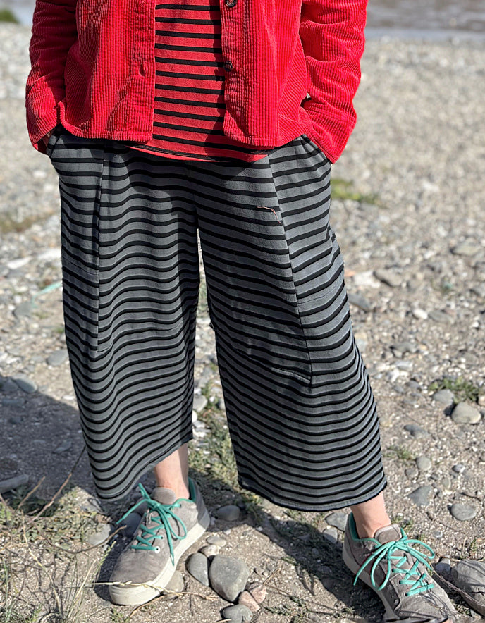 Person wearing a red jacket, striped shirt, and wide-leg pants standing on a rocky ground.