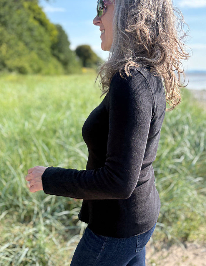 Person wearing a black long-sleeve shirt and sunglasses standing outdoors with grass and water in the background