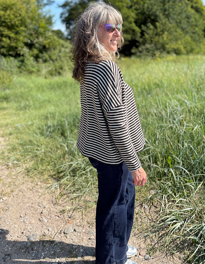 Woman wearing a black and white striped shirt and sunglasses in a grassy field.