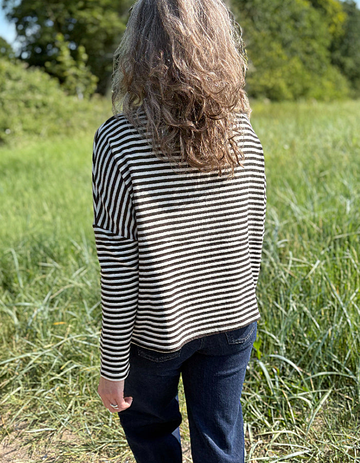 Woman wearing a black and white striped shirt and sunglasses in a grassy field.