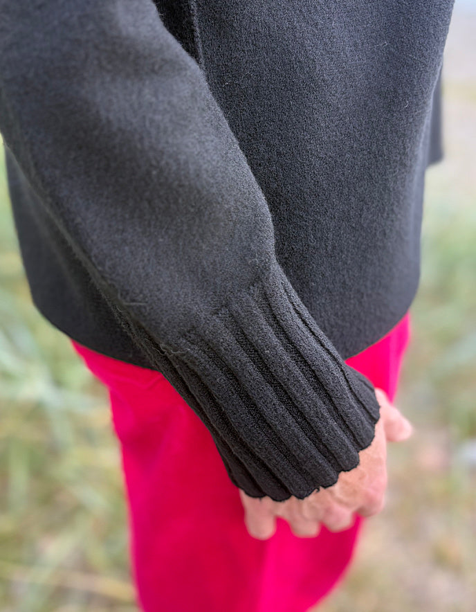 Person wearing a black turtle neck sweater and pink velvet pants standing on a beach.