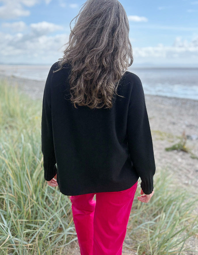 Person wearing a black turtle neck sweater and pink velvet pants standing on a beach.