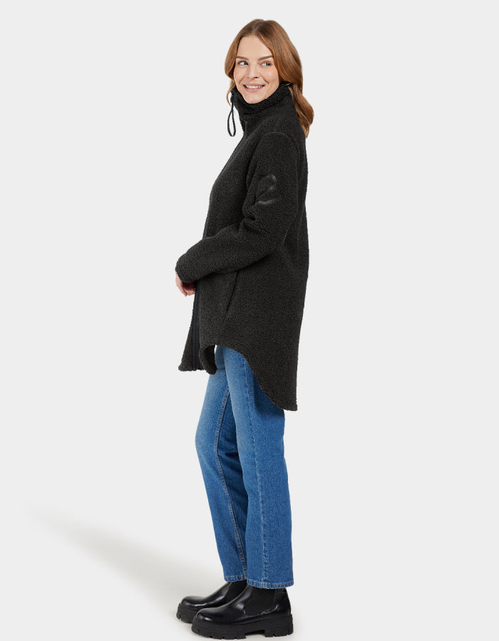 A woman smiling, wearing a black full zip fleece jacket with a stand-up turtle neck and curved hemline. The jacket is displayed on a plain background.