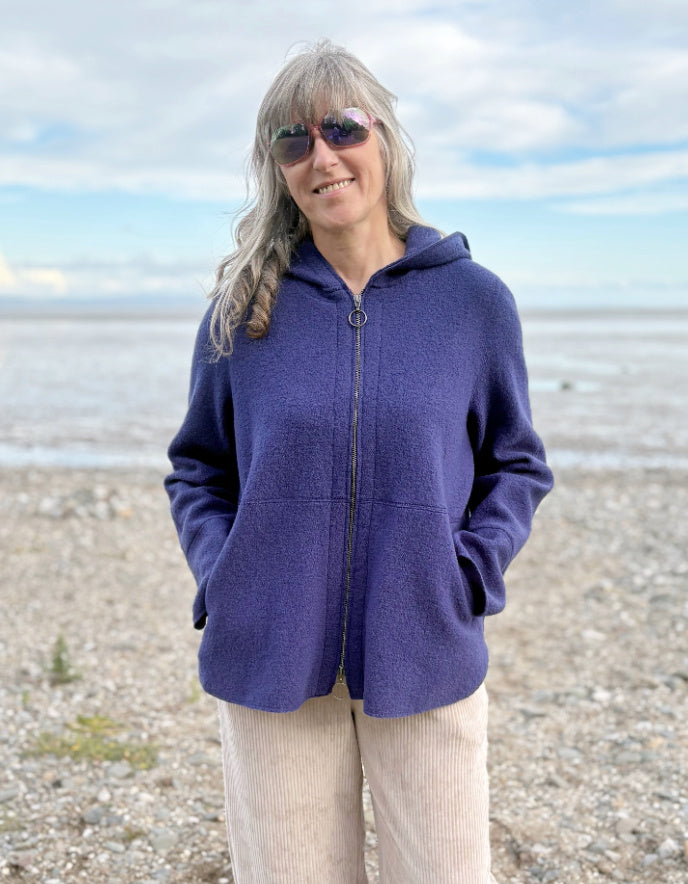 Person wearing a blue hooded boiled wool jacket on a beach