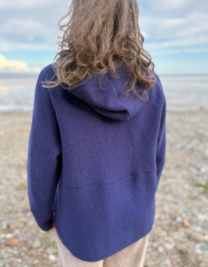 Person wearing a blue hooded boiled wool jacket on a beach