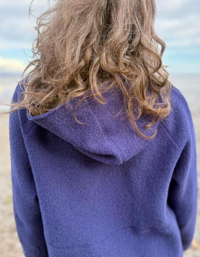 Person wearing a blue hooded boiled wool jacket on a beach