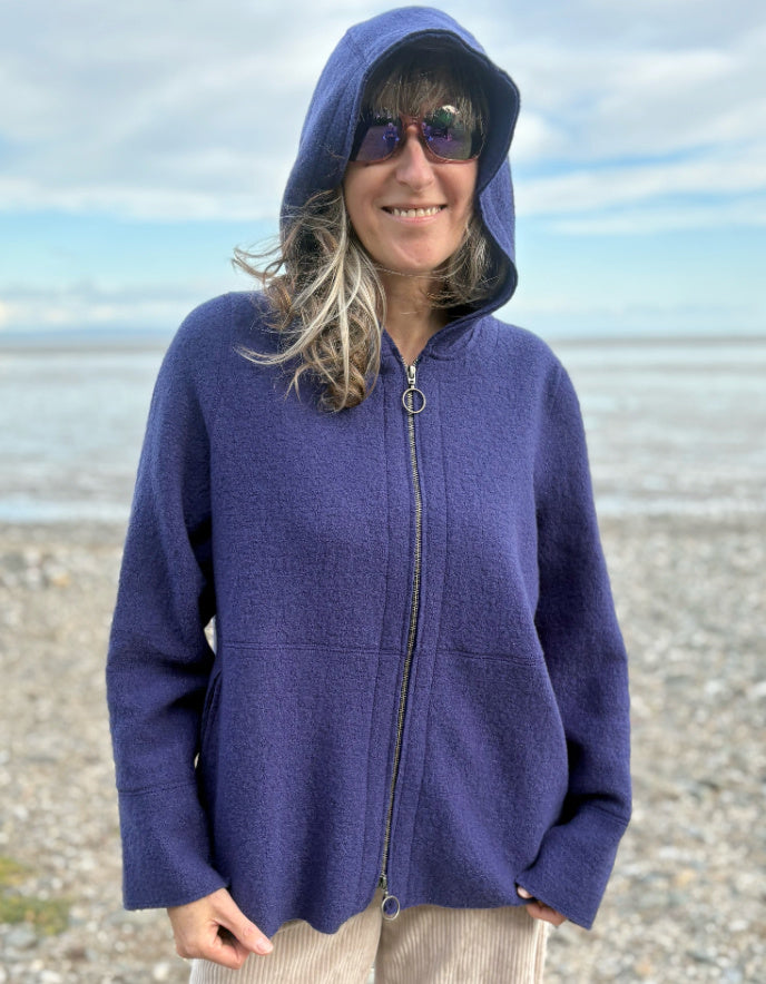 Person wearing a blue hooded boiled wool jacket on a beach
