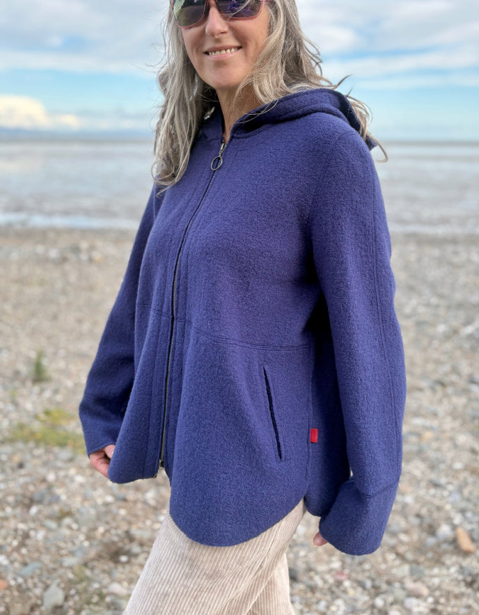 Person wearing a blue hooded boiled wool jacket on a beach