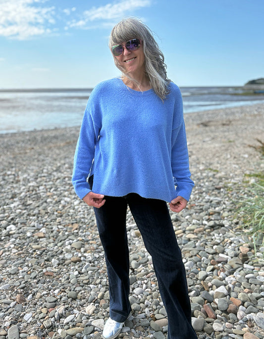 Person wearing a blue sweater and sunglasses on a pebbly beach.