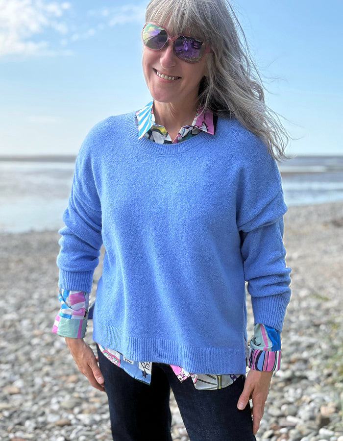 Woman wearing a blue sweater and colorful shirt on a beach
