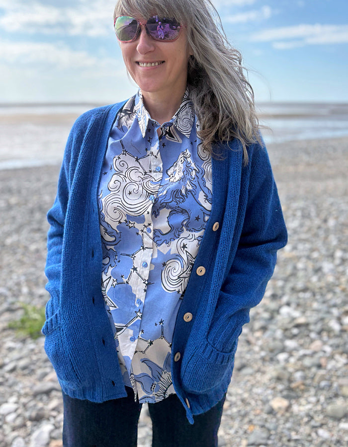 Person wearing a blue cardigan and patterned shirt on a beach