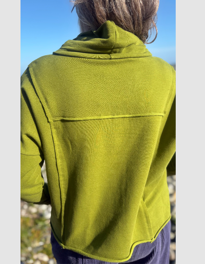 A person viewed from behind wearing an olive green cropped hoodie or lightweight jacket outdoors under a blue sky.