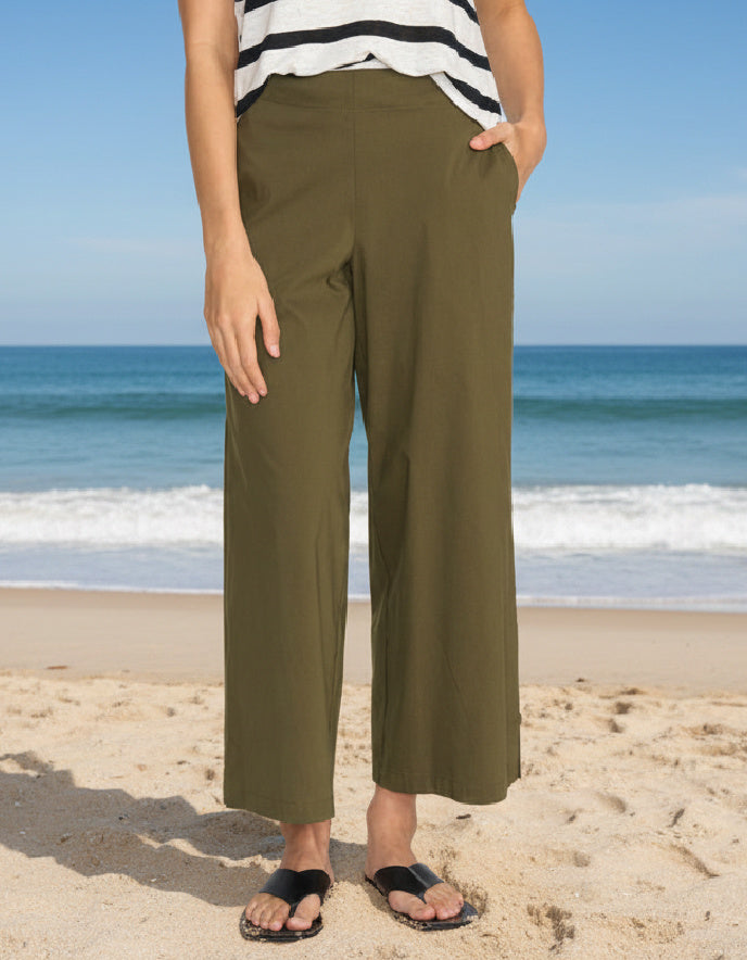 Person wearing olive green pants and a striped shirt on a beach.