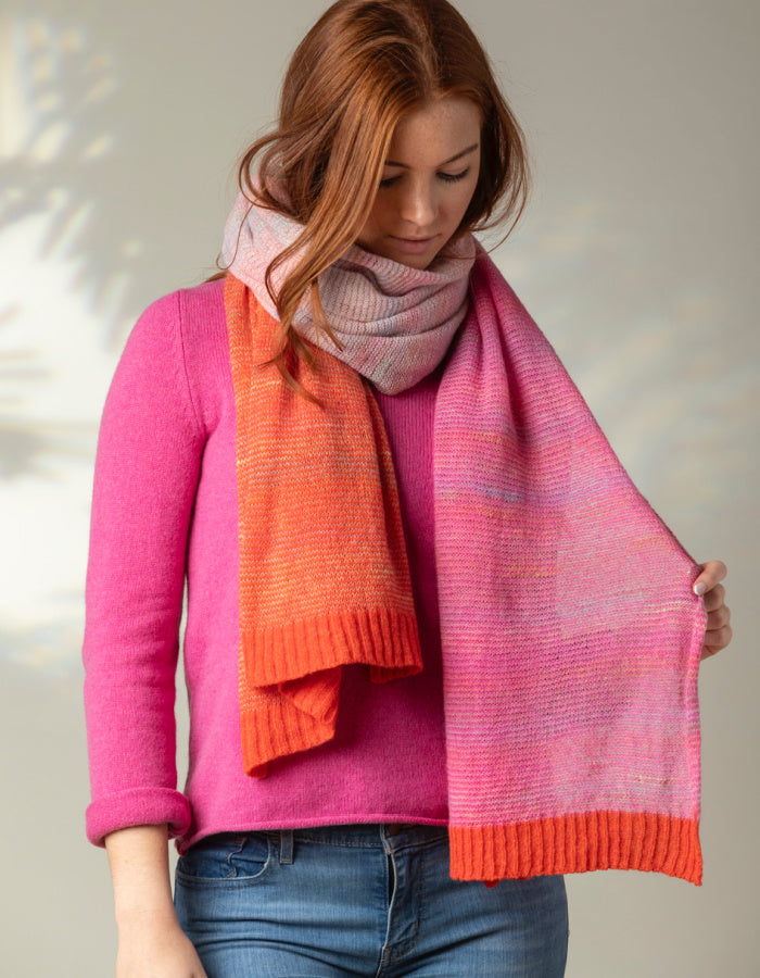 A person wearing a pink and orange striped scarf with a knit texture, draped over the shoulders.