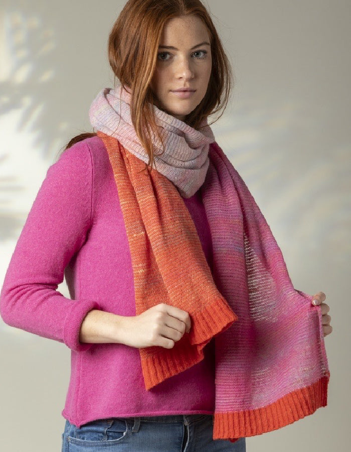 A person wearing a pink and orange striped scarf with a knit texture, draped over the shoulders.