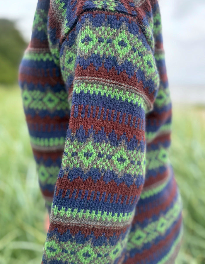 Close-up of a colorful knitted sweater sleeve with a pattern against a blurred natural background.