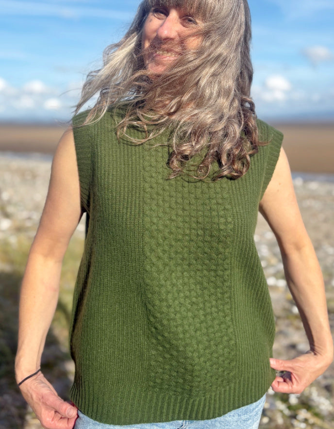 Person wearing a green sleeveless knitted sweater on a beach