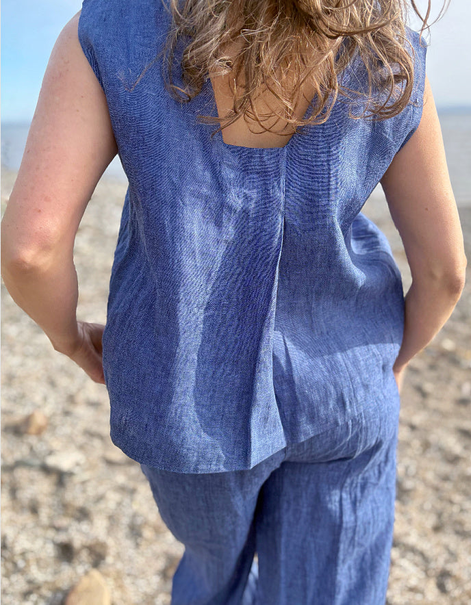 Person wearing a blue sleeveless top and pants on a beach.