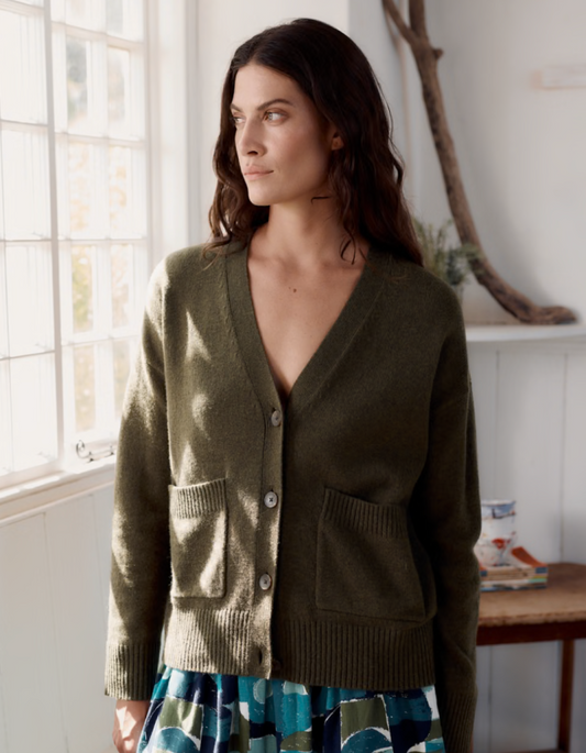 Woman wearing a green cardigan in a bright room with large windows.