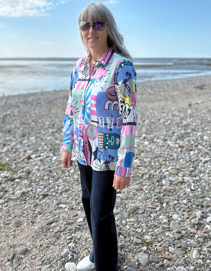 Woman wearing a colorful patterned shirt on a pebbly beach.