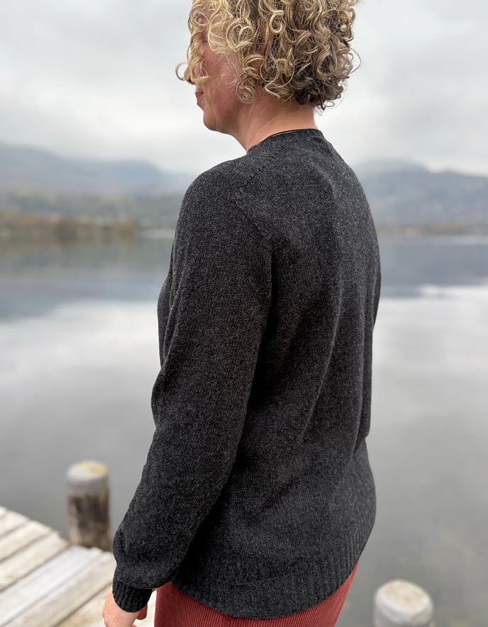 Person wearing a dark gray sweater by a lake with mountains in the background