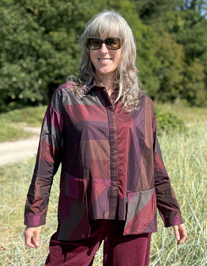 Woman wearing a check taffeta shirt and burgundy velvet pants standing in a field with trees in the background