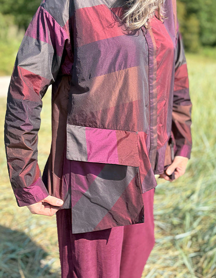 Woman wearing a check taffeta shirt and burgundy velvet pants standing in a field with trees in the background