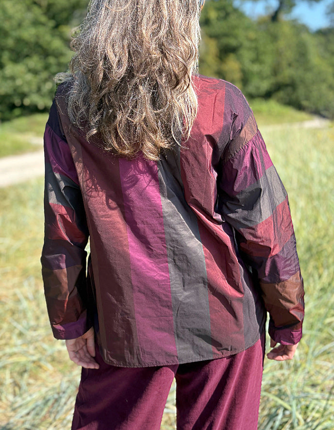 Woman wearing a check taffeta shirt and burgundy velvet pants standing in a field with trees in the background