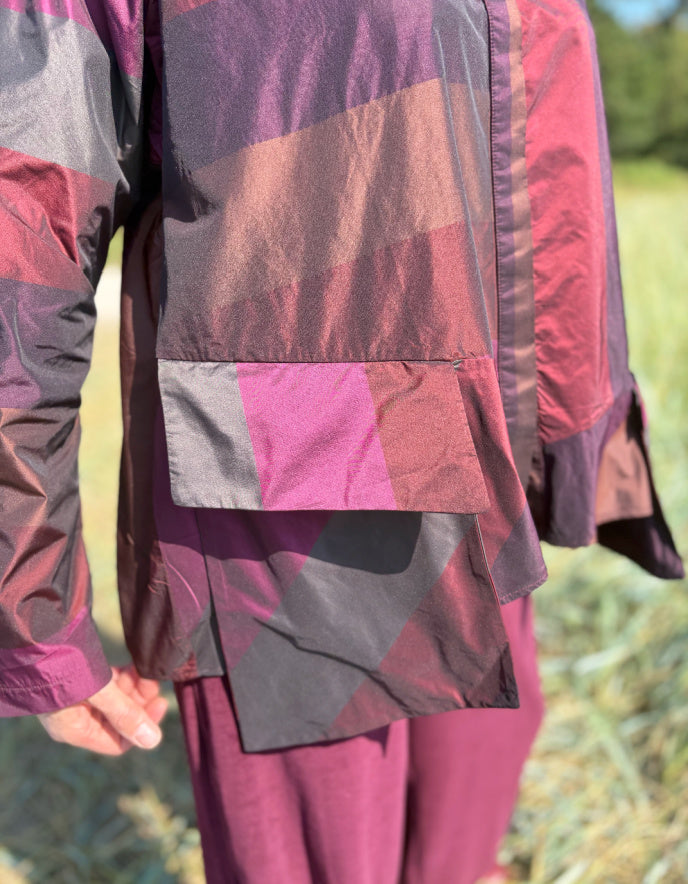 Woman wearing a check taffeta shirt and burgundy velvet pants standing in a field with trees in the background