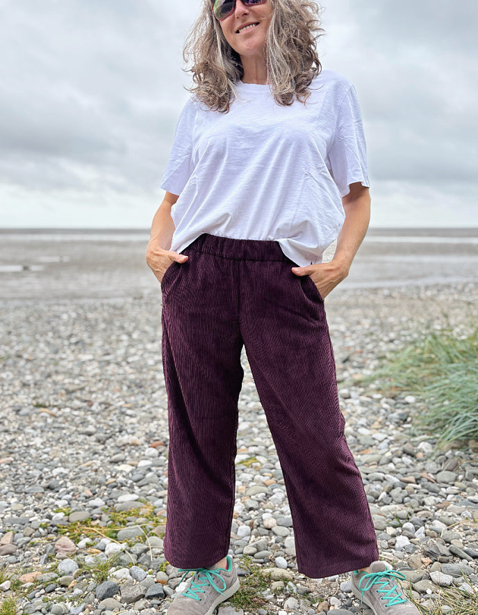Person wearing a white t-shirt and burgundy pants standing on a pebbly beach.