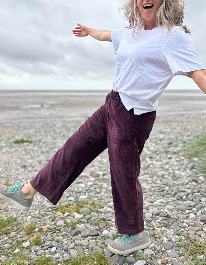 Person in white shirt and purple pants on a pebbly beach
