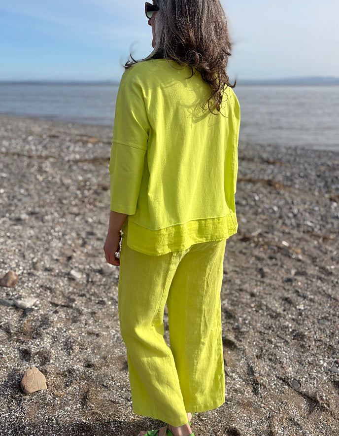 Person wearing a bright yellow outfit standing on a pebbly beach with ocean in the background