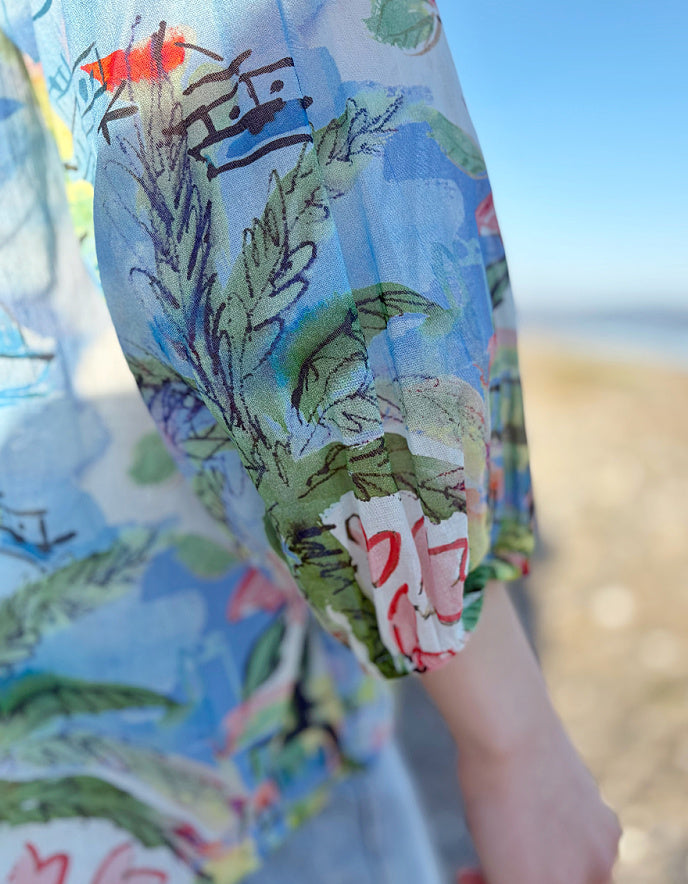 Woman wearing a colourful coastal print cotton shirt with a beach-themed design on a beach.