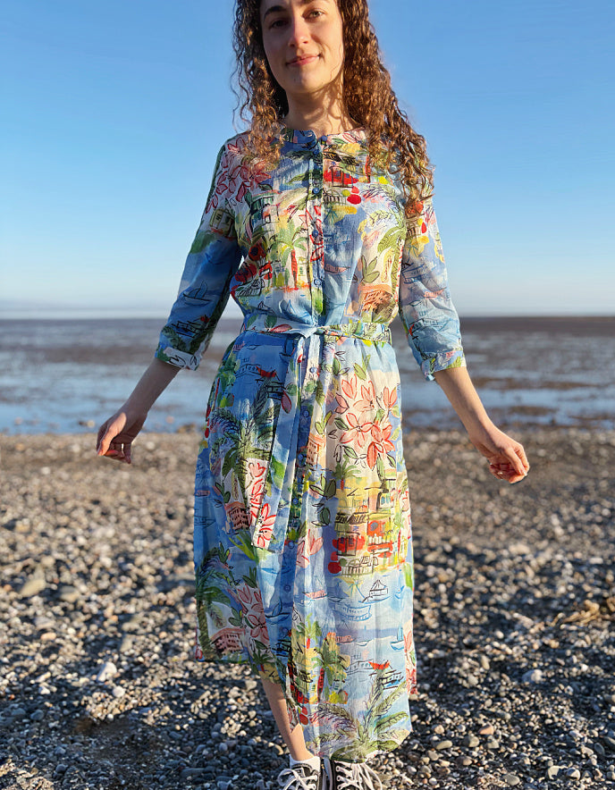 Woman in a colorful dress standing on a pebbly beach with ocean in the background