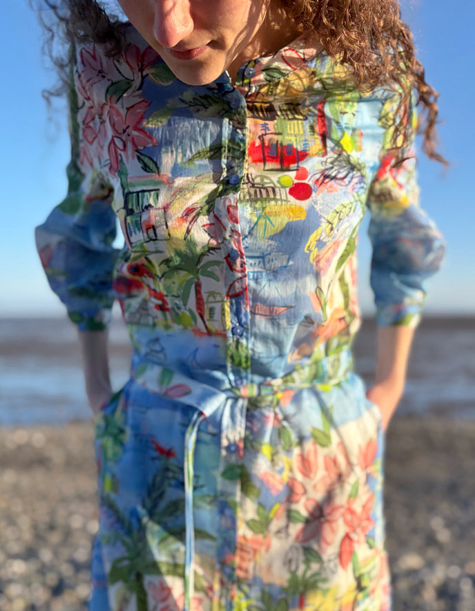 Person wearing a colorful dress with a pattern of houses and flowers on a beach.
