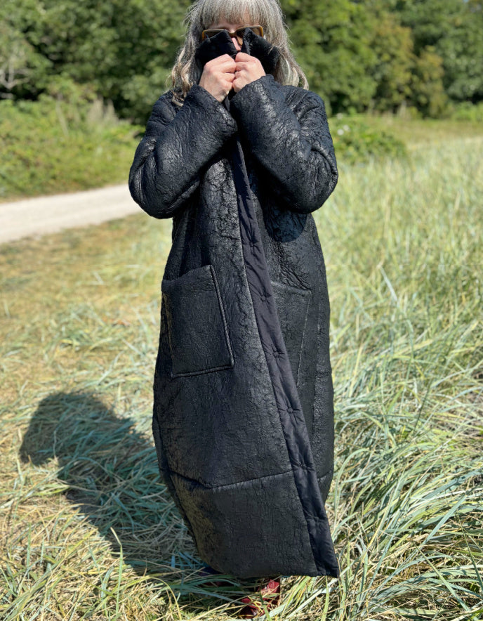 Person wearing a long black coat standing in a grassy field.